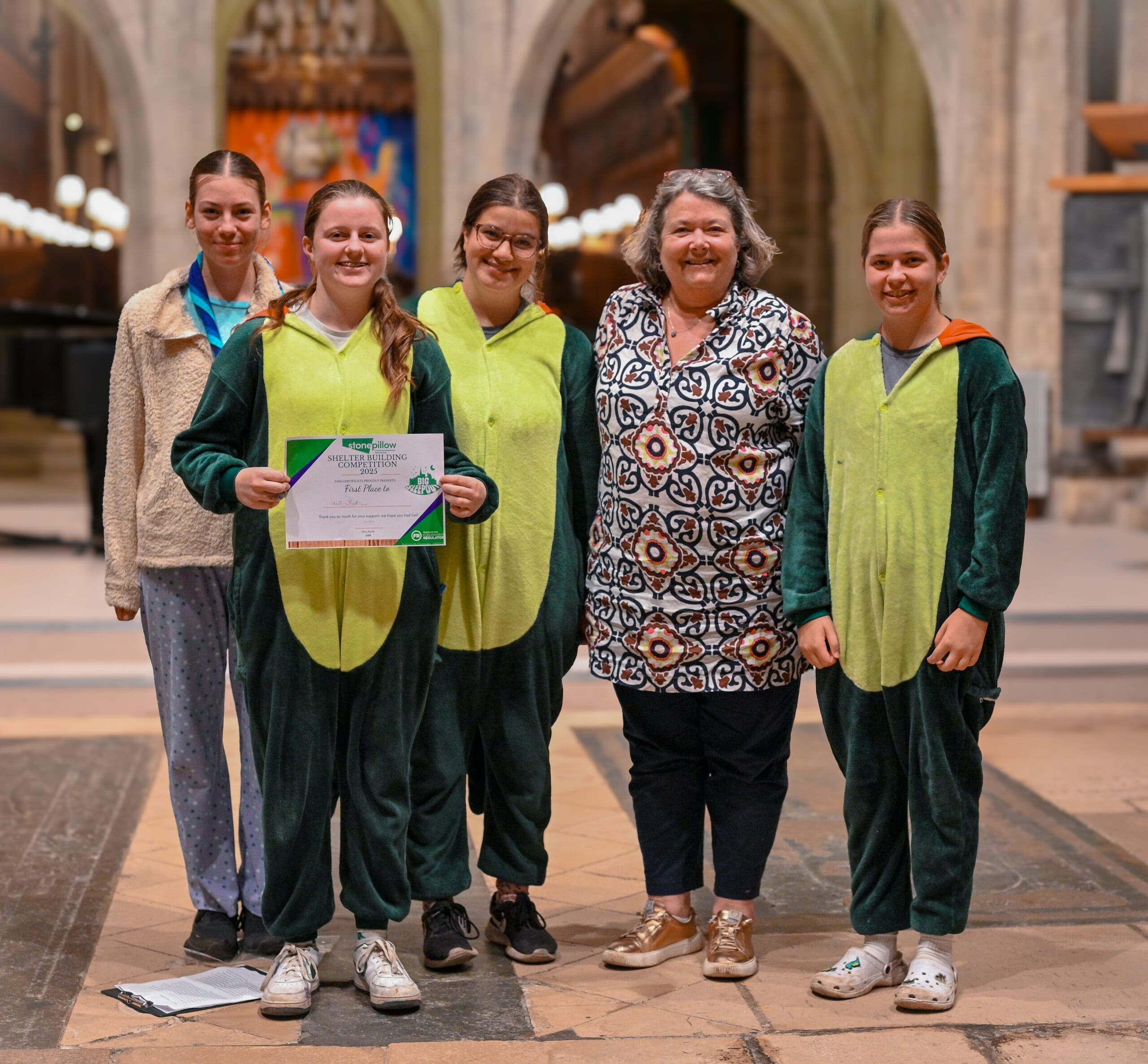 A group of smiling young people in dinosaur onesies holding a certificate stand with CEO Hilary Bartle.